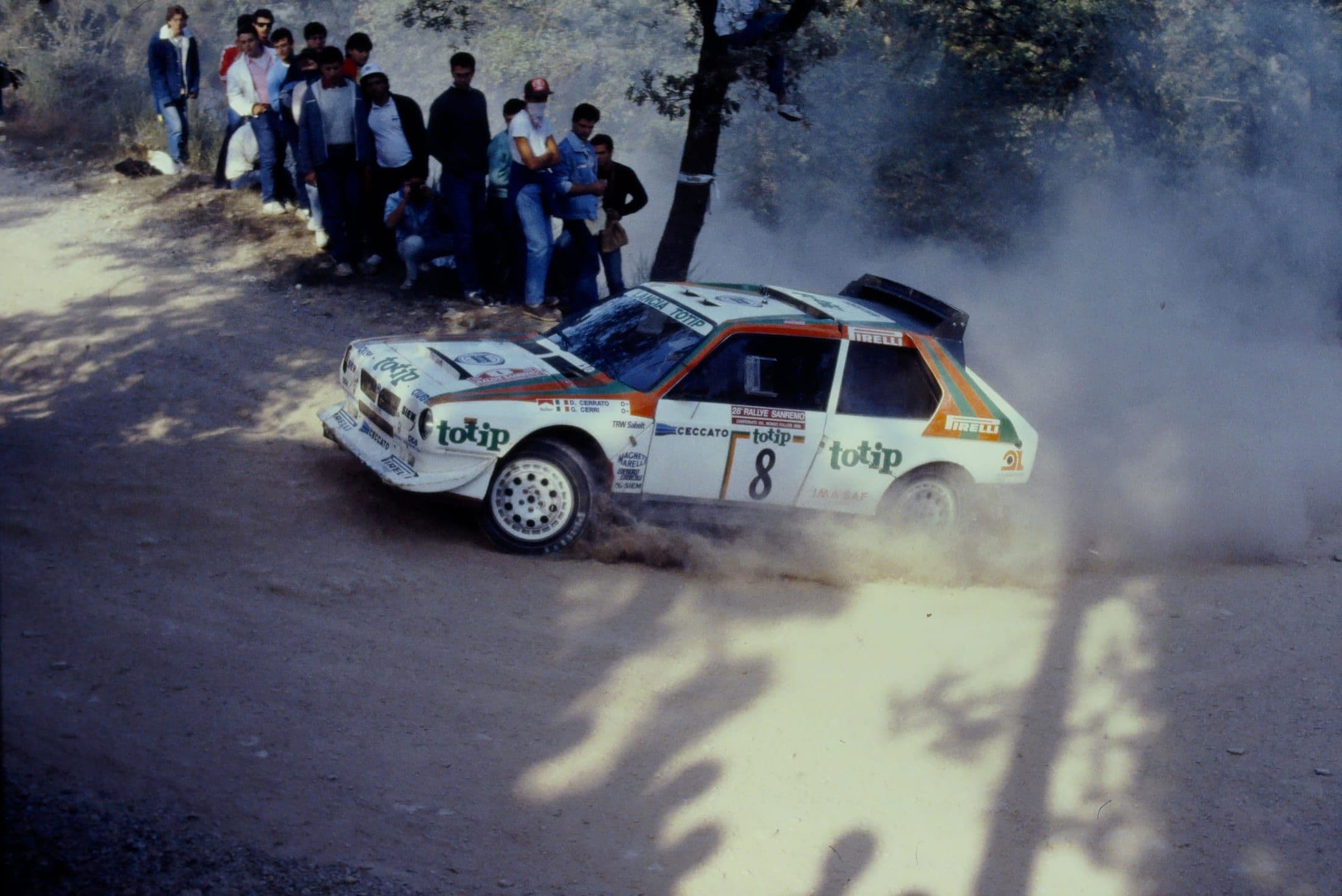 A Group B-era Lancia rally car competing on a dirt stage in the 1980s